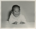 An African American baby dressed in white clothing and a white bow by Lonnie W. Fleming Sr.