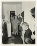 An elderly woman walks in through a doorway carrying a raincap by Lonnie W. Fleming Sr.