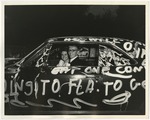 Photo of a bride and groom in their car that is covered in white writing by Lonnie W. Fleming Sr.