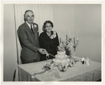 Photo of an elderly couple cutting a cake while looking straight at the camera by Lonnie W. Fleming Sr.