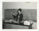 Photo of a female holding up a scalpel in the front of a class by Lonnie W. Fleming Sr.