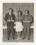 A photo of two gentlemen and a lady posing with trophies in front of a table with chairs by Lonnie W. Fleming Sr.