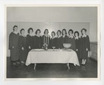 A photo of a row of gowned individuals posing behind a clothed table with three lit candles by Lonnie W. Fleming Sr.