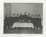 A photo of a row of gowned students behind a clothed table with four lit candles by Lonnie W. Fleming Sr.