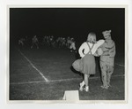 A photo of a cheerleader and a tiger mascot leaning on each other and watching a football match by Lonnie W. Fleming Sr.