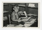 A photo of a little boy smiling while holding a yearbook and a bookmark by Lonnie W. Fleming Sr.
