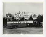 A photo of a twelve wheeler oil truck that says "American" on it underneath large oil containers by Lonnie W. Fleming Sr.