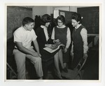 A group of four students looking at a magazine by Lonnie W. Fleming Sr.