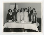 A photo of seven people (1 male and 6 females) posing behind a table with cake on it by Lonnie W. Fleming Sr.
