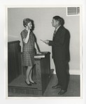 A woman swearing an oath and a gentleman presenting a piece of paper to her by Lonnie W. Fleming Sr.