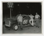 Three men posing by an old race car with 66 painted on it by Lonnie W. Fleming Sr.