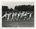 A photo of girls in overall dresses with the letter "L" on them kneeling in the grass and their arms spread by Lonnie W. Fleming Sr.