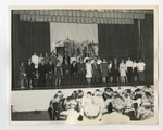 A group of students putting on an urban-set play on the stage of an auditorium by Lonnie W. Fleming Sr.