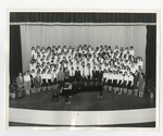 A group of dressed up students taking a group picture on stage behind a piano by Lonnie W. Fleming Sr.
