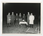 Seven gentlemen in coats standing around a trophy on a football field by Lonnie W. Fleming Sr.